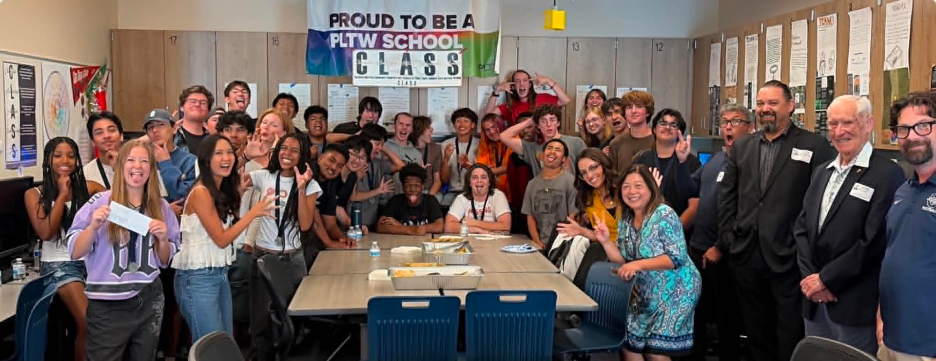Guia Blaske with her full PLTW engineering class of 2026, students and district guests packed into the classroom, smiling under a Proud to be a PLTW School banner